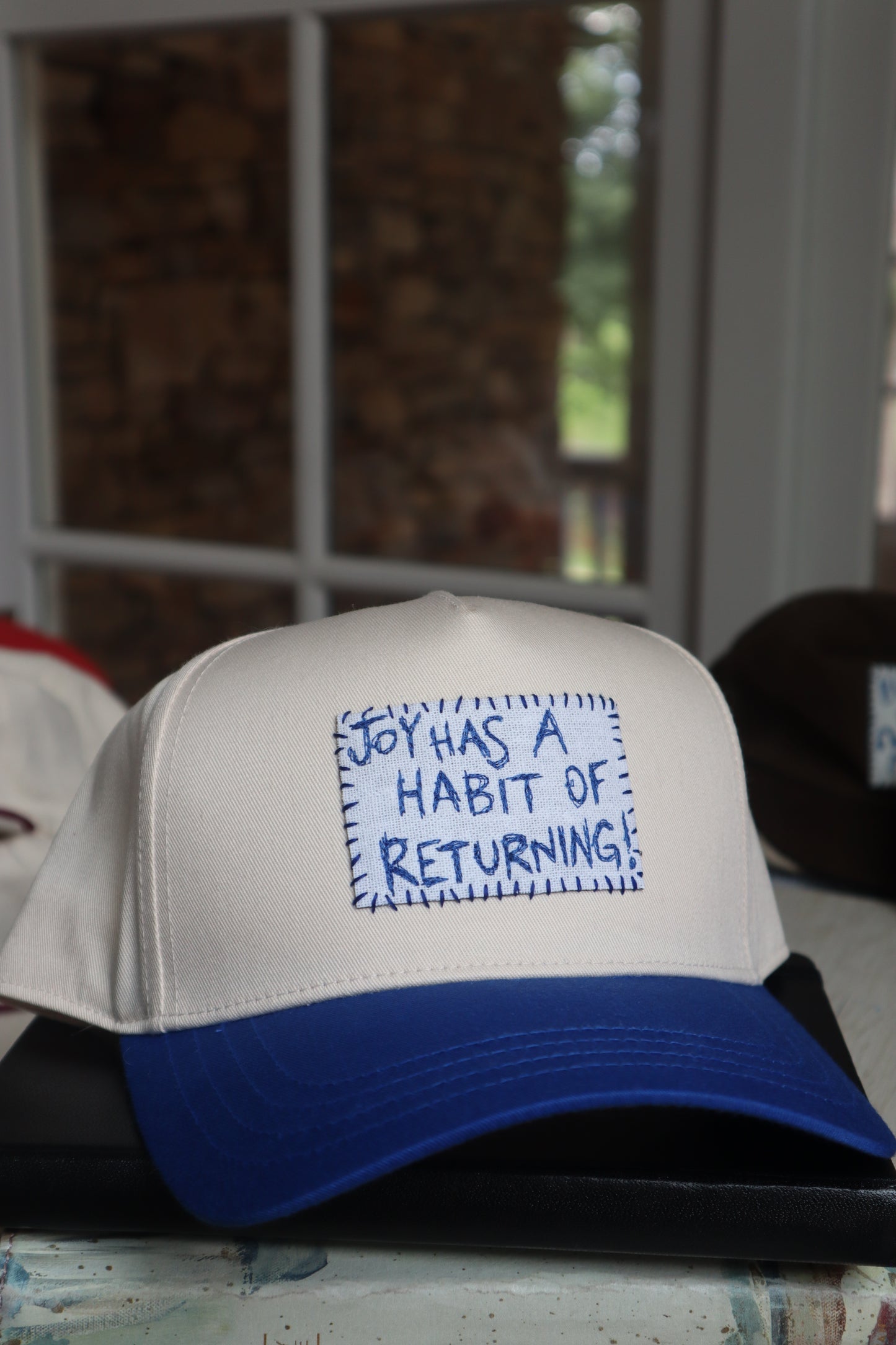 "joy has a habit of returning" - blue trucker hat